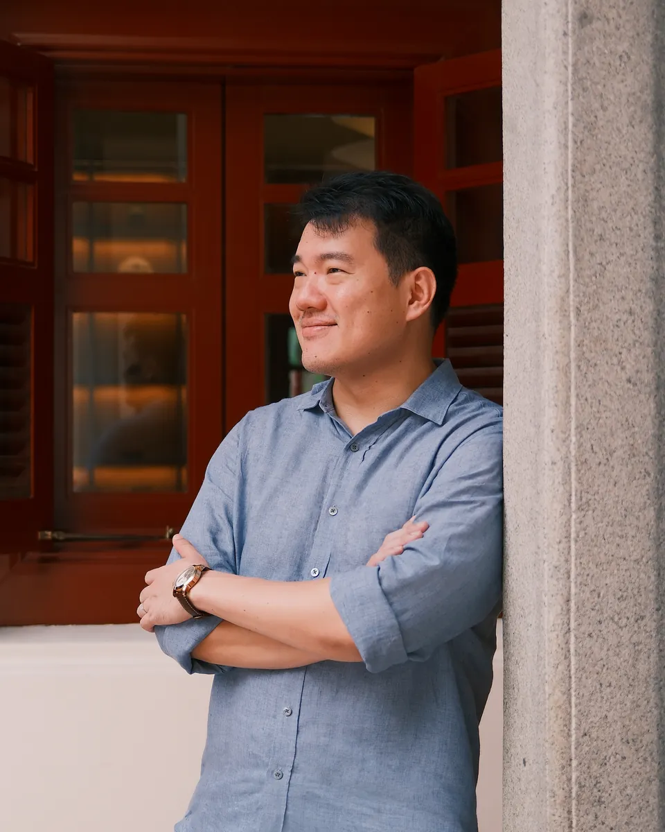 Sean Chan, smiling with his arms crossed, beside an open red lacquered window